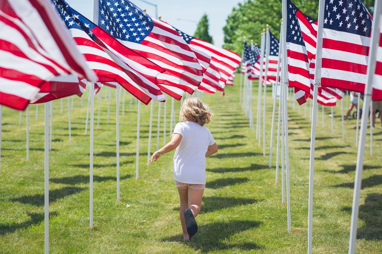 Joyful child runs through a display of American flags on a sunny day, capturing freedom and innocence.