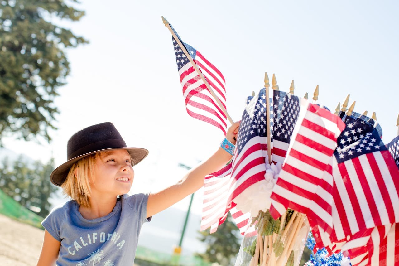 A joyful child celebrates with American flags outdoors on Independence Day.