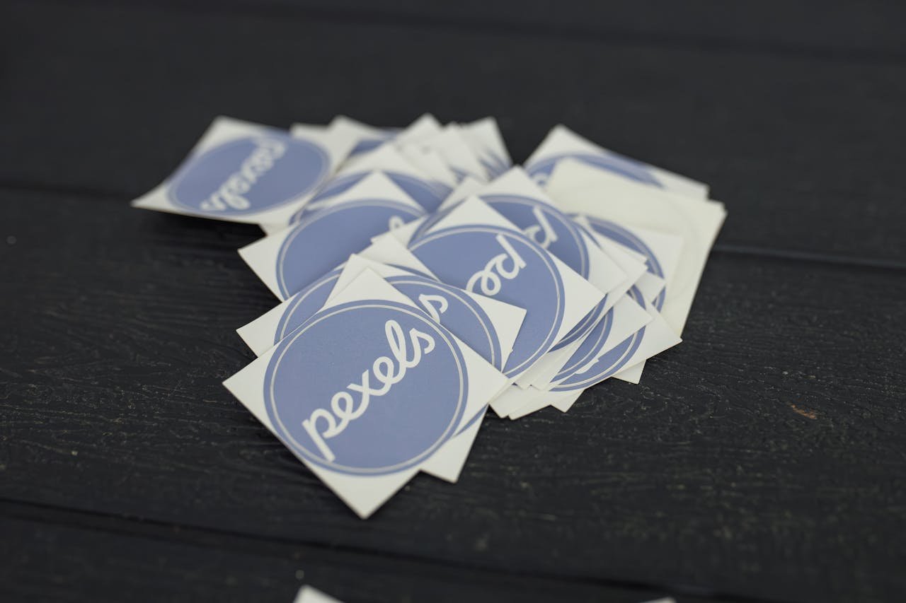 A pile of Pexels logo stickers arranged on a dark wooden surface.